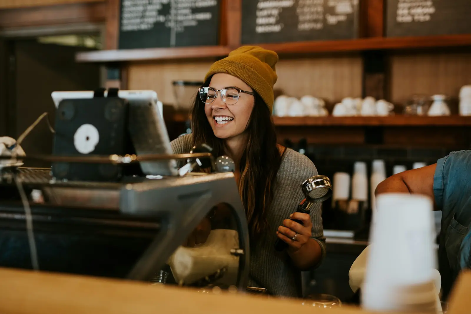 Mujer sonriendo tras la barra de una cafetería, junto a la cafetera