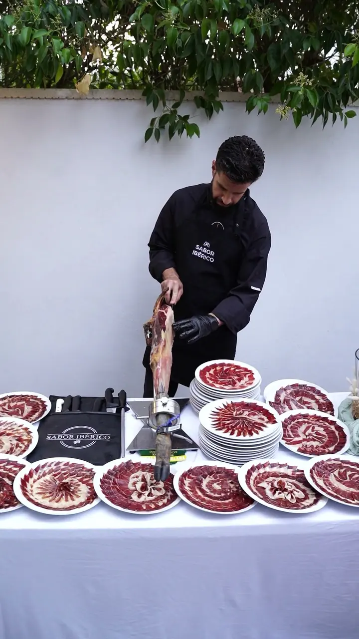Mesa con platos de jamón recién cortado y el cortador trabajando en una boda