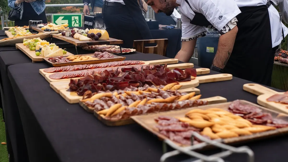 Mesa de catering de Sabor Ibérico con tablas de embutido y queso, y un camarero preparándola