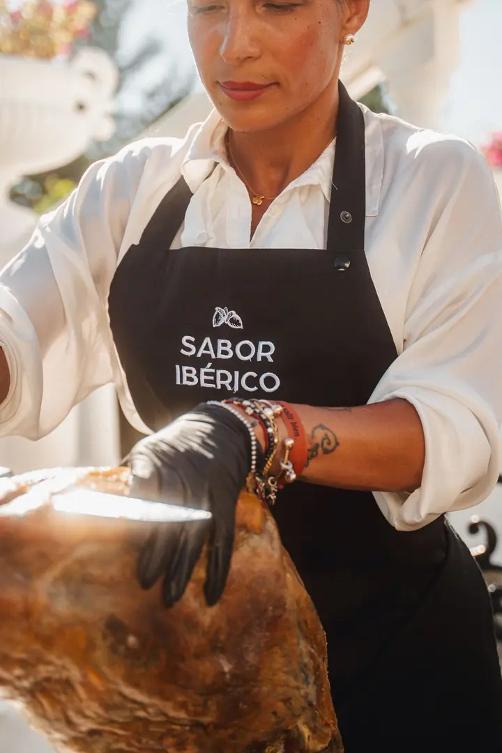 Cortadora de jamón con delantal de Sabor Ibérico junto a la pata de jamón en un evento